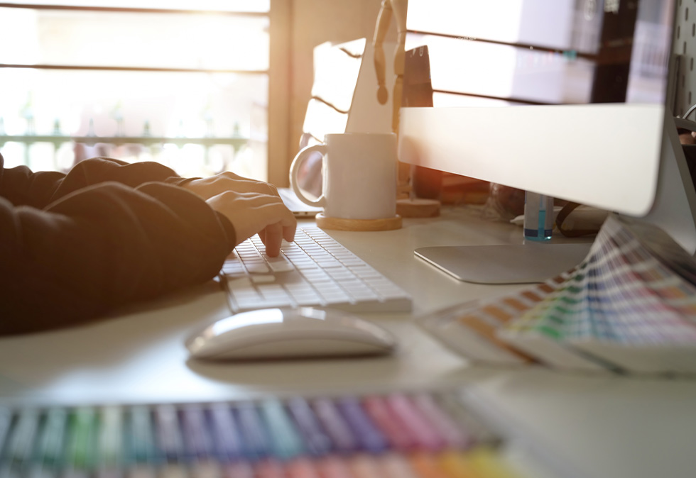 person's hands on keyboard with monitor and color swatches on table for a blog about Choosing the Right Full-Service Agency