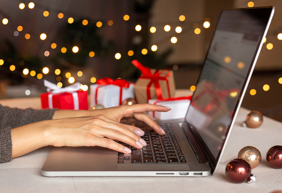 person working on laptop with holiday presents in background for a blog about ad spend tracking during the holidays