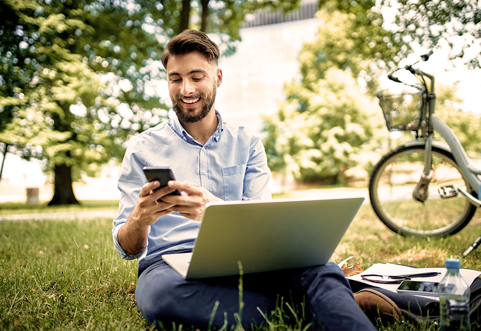 Man sitting in the park with his phone and laptop for a post about how to do a Digital Marketing Audit for your brands
