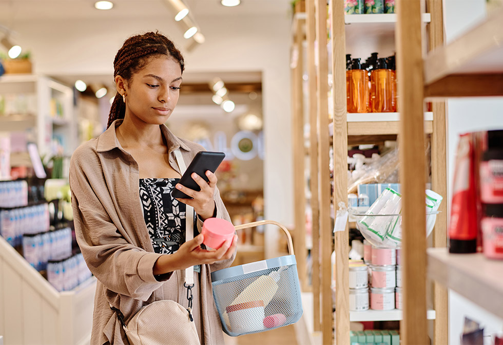 girl shopping in store holding product in one hand and looking at her phone in her other hand for a blog about How Strategy Shapes Customer Loyalty and Retention in 2026